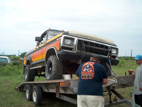 1979 Ford F-Series truck on a trailer, orange and black stripe, lifted, bull bar, two men nearby