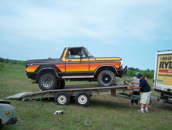Orange and yellow 1978 Ford Bronco on a trailer, being loaded by two men