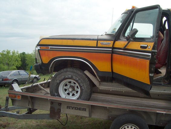 1978 Ford Bronco with orange and yellow stripes on a trailer, another car visible behind it