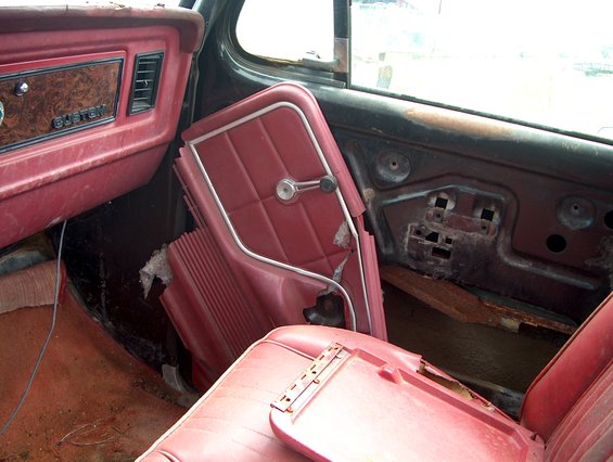 Red interior of a 1979 Ford Bronco with a broken door panel and wood-grain trim