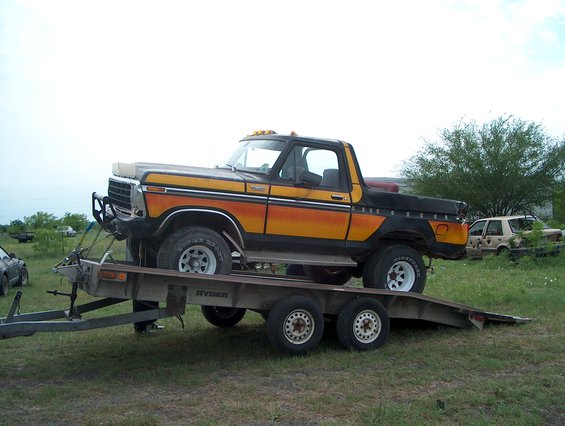 Ford Bronco on a trailer, orange and black paint scheme. Another car in background