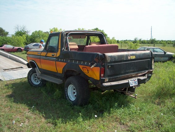 1979 Ford Bronco with orange and black stripes, rear view. Another car is parked behind it
