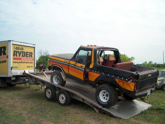Ford Bronco on a trailer, Ryder truck nearby. Bronco has orange and black stripes