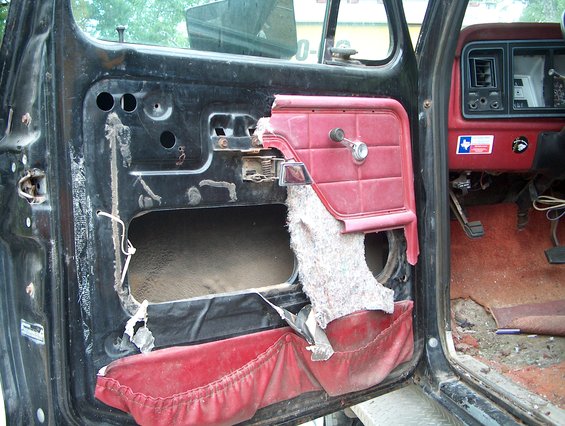 Damaged red and black interior of a 1979 Ford Bronco, showing a torn door panel and worn dashboard