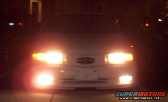 Front view of a white car at night with headlights illuminated