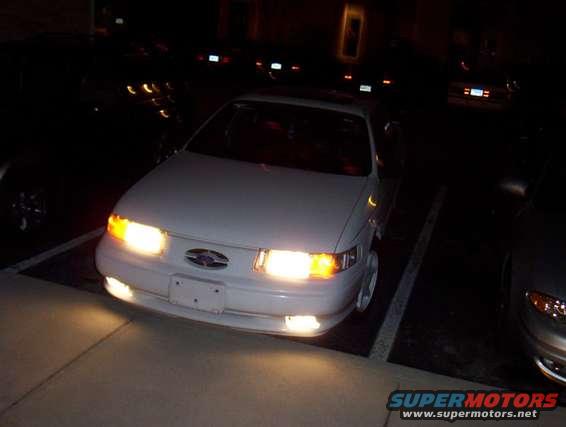 1993 Ford Taurus parked at night, headlights on. Another car is visible to the right