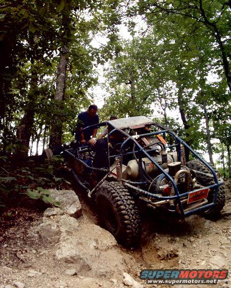 Blue off-road buggy with exposed engine and roll cage climbing a rocky incline
