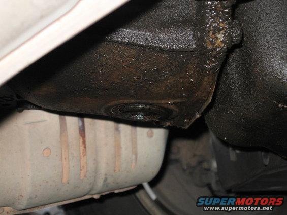Underside of a vehicle showing an oily transmission housing and a catalytic converter