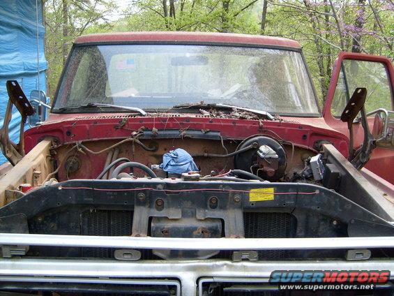 Red Ford truck engine bay with hood open, showing engine components and a blue cloth. Grille reads "FORD"