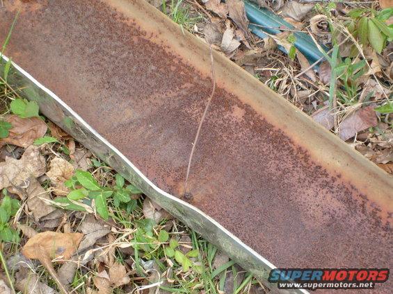 rusted metal pipe with a crack, lying on the ground with leaves and grass