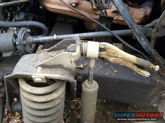Engine bay component held by vice grips, with coil spring and shock absorber visible