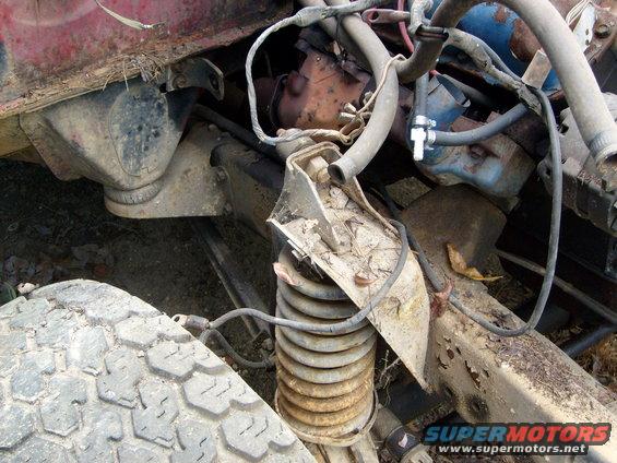 Engine and suspension parts of a rusty vehicle, showing a coil spring and hoses