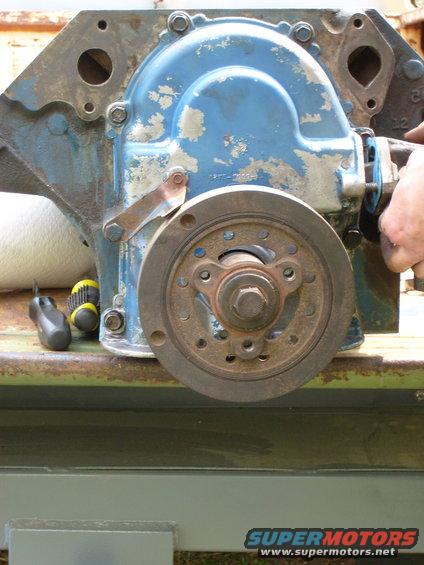 Blue engine timing cover with a pulley attached, resting on a metal surface. Tools are nearby