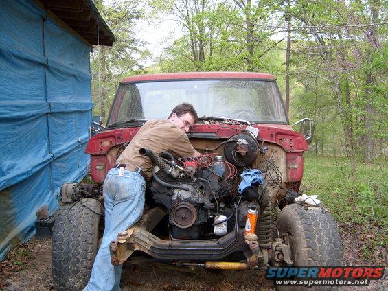 guy bent over working on the engine of a red truck that's missing its hood and fenders