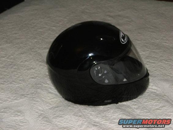 Black motorcycle helmet with clear visor, resting on a textured surface