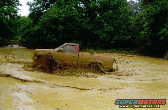 Mud-splattered pickup truck driving through a muddy water obstacle