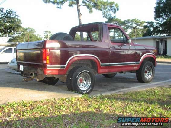 Maroon 1980s Ford Bronco with a spare tire mounted inside. The vehicle is parked on a paved surface next to a grassy area