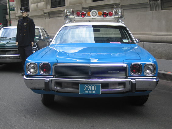 Blue police car with light bar, NYC Police license plate 2900, parked next to a mannequin in uniform