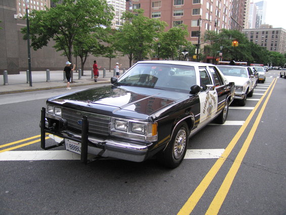 Black and white 1991 Ford Crown Victoria police car, front 3/4 view, with push bumper and light bar
