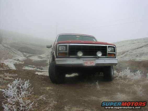 Front view of a red pickup truck with a black grille and "FIRE DEPT" plate, parked on a dirt road in foggy conditions
