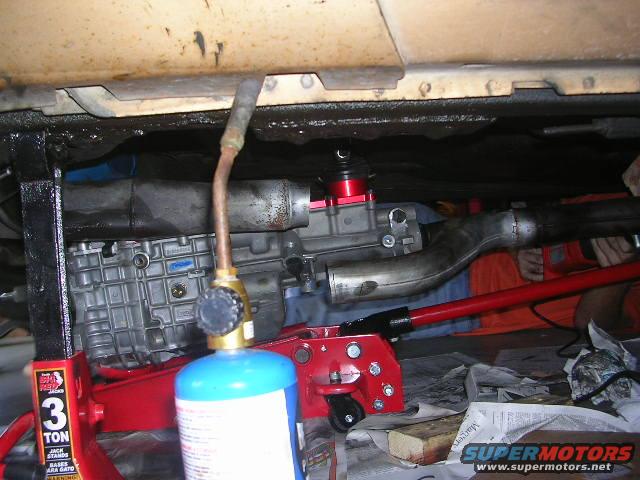 Undercarriage of a vehicle with a transmission, exhaust pipe, and a propane torch on a jack stand