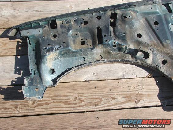 Green fender frame with holes and rust, sitting on wooden planks