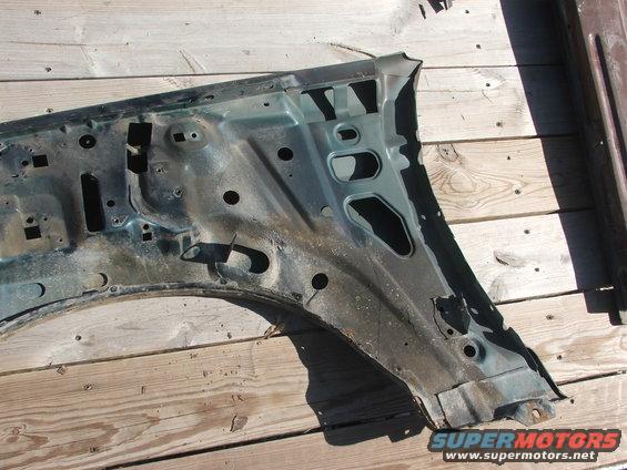 Green metal fender well structure with rust and holes, lying on wooden planks