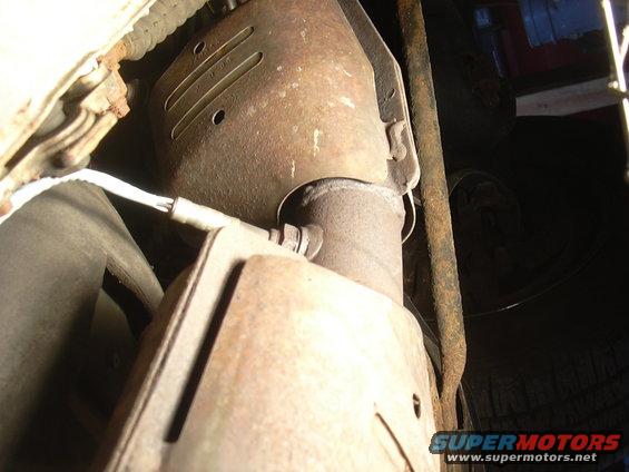 Close-up of a rusty catalytic converter and exhaust pipe with an oxygen sensor attached