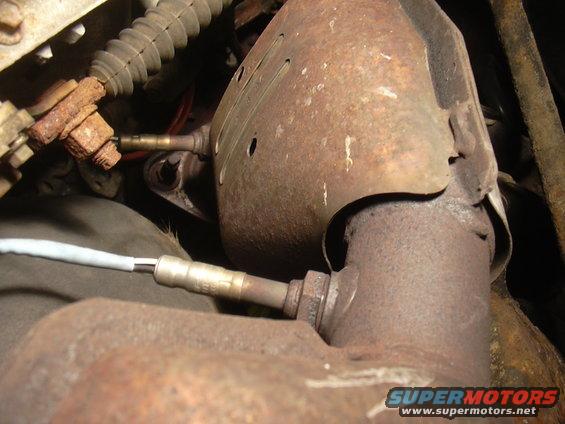Close-up of rusty catalytic converter with two oxygen sensors attached. One sensor wire is white