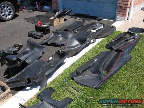 Car interior trim pieces and floor mats spread on driveway and grass