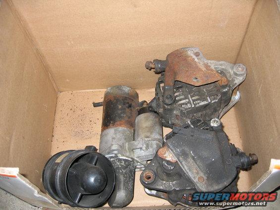 Box of assorted used car parts including starters and an alternator