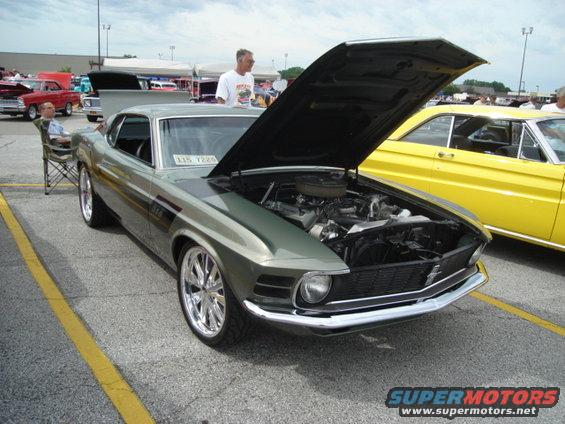 Green 1969 Ford Mustang Boss 302 with hood open, parked next to a yellow car