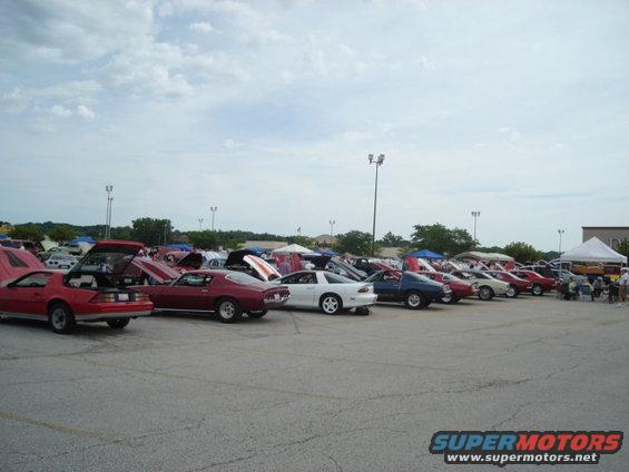 Cars parked in rows at an outdoor event, some with hoods open