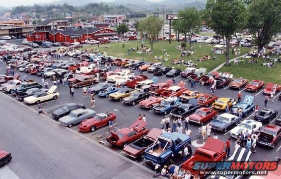 Outdoor car show with rows of classic cars and people milling about