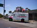 1989 Ford Bronco - A white truck advertising 'La Pulga Flea Market' drives down the street with several flags on its roof.