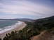 1989 Ford Bronco - A scenic view of a wide, populated beach stretching along the coast, bordered by lush green hills and the blue ocean.