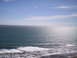 1989 Ford Bronco - The sun reflects off the deep blue ocean as waves roll towards a dark, rocky beach.