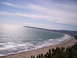 1989 Ford Bronco - A scenic coastal view captures the expanse of the ocean meeting a populated beach, with rolling hills in the background.