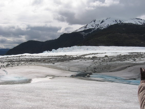 Glacier scene with snow-capped mountains and a person's gloved hand in the foreground