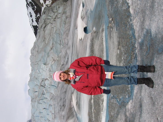 Person in red jacket and pink hat standing on a glacier with ice formations behind them