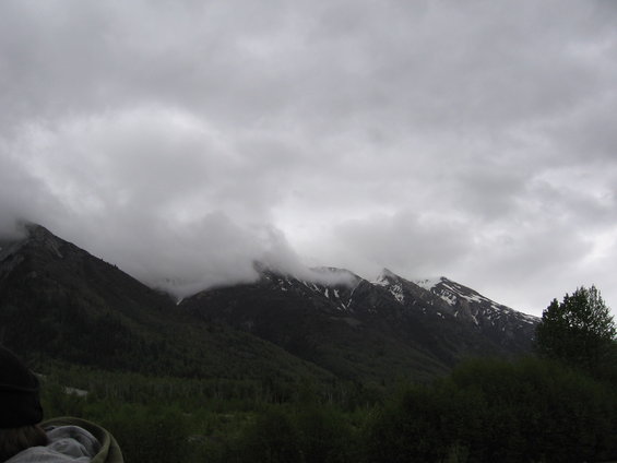 cloudy sky over forested mountains with some snow on peaks