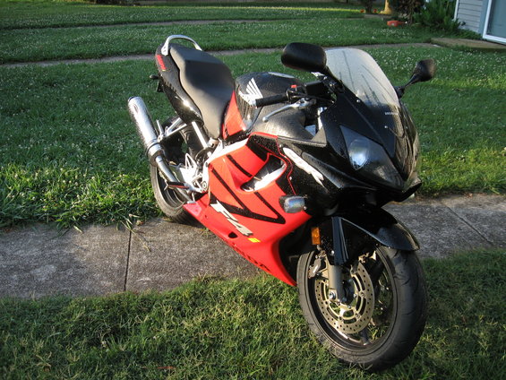 Red and black sportbike parked on a sidewalk next to grass