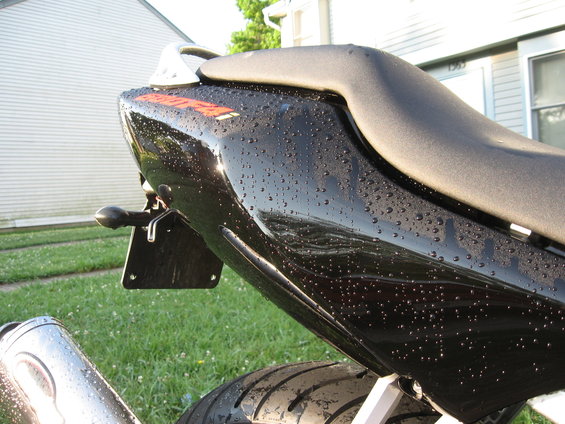 Black motorcycle tail section with water droplets, close-up rear view
