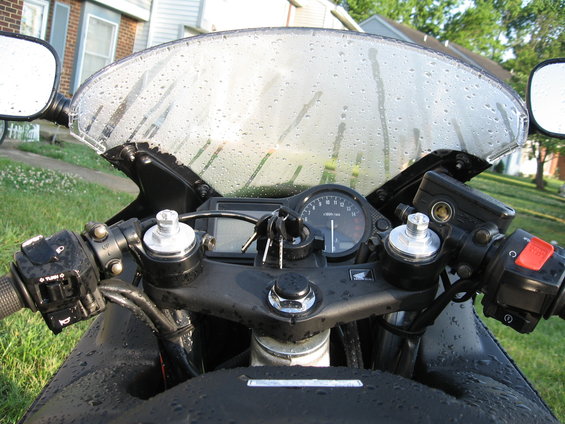 Motorcycle dashboard with keys in ignition, tachometer, and windshield covered in water droplets