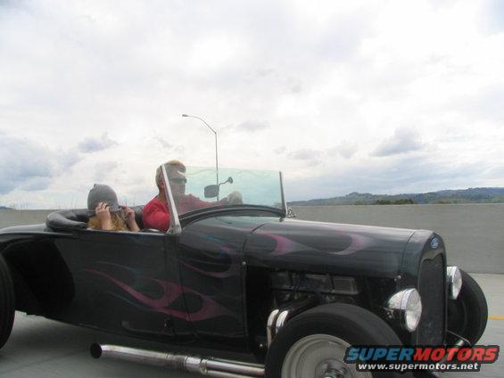 Black hot rod roadster with pink flames, two people inside