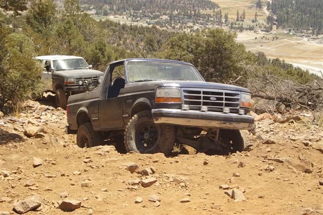 Dark blue Ford Bronco navigating a rocky trail, with another SUV behind it