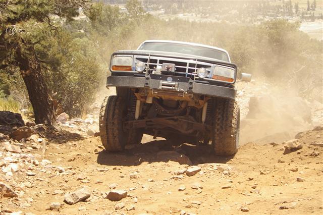 Front view of a lifted Ford F-Series truck with a winch, driving on a dusty, rocky trail