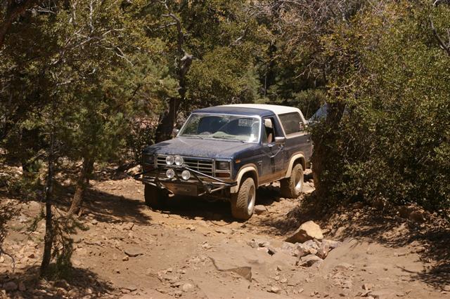 1986 Ford Bronco on a rocky trail, dark blue with white top