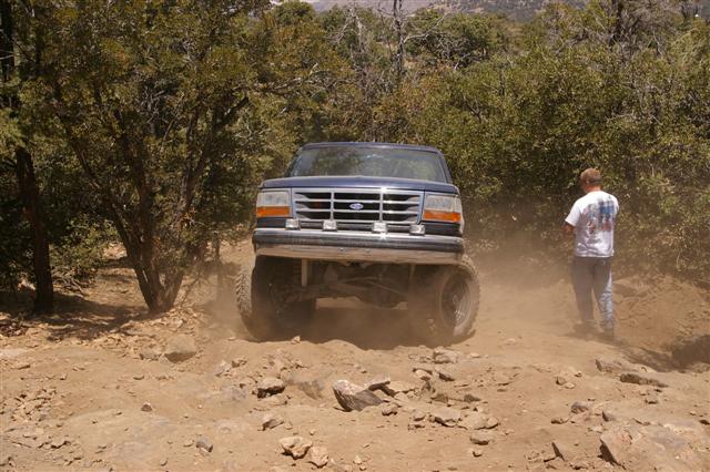 Blue Ford Bronco on a rocky, off-road trail with a person standing to the right