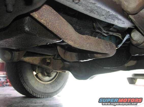 Underside view of vehicle suspension, showing a tire and rusty metal components